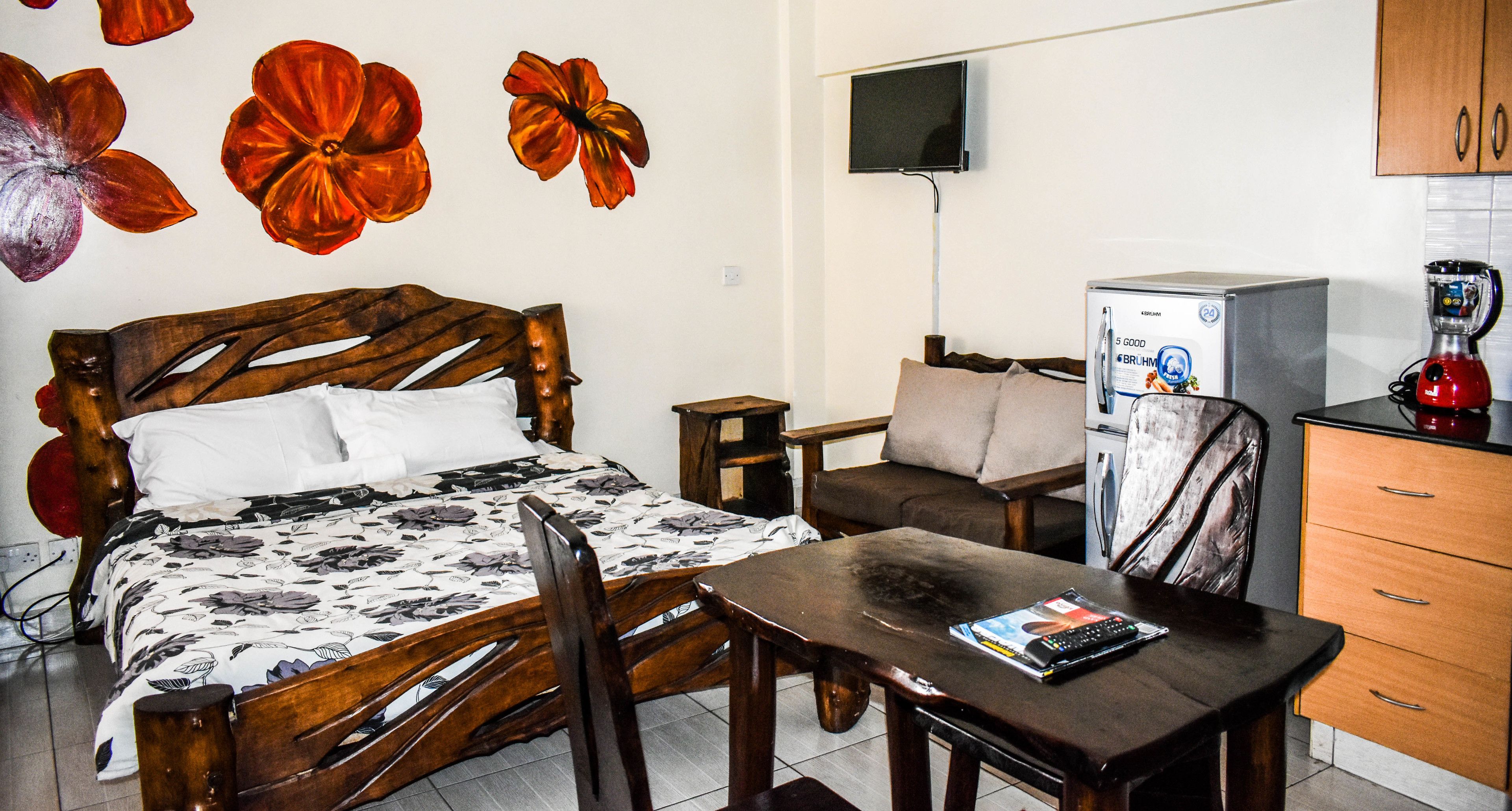 A room with a bed, a desk, a chair, a television, a refrigerator, and a coffee maker.