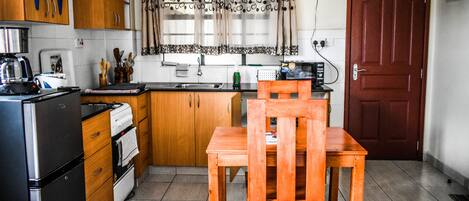 Une cuisine compacte dotée de meubles en bois, d’un réfrigérateur, d’une cuisinière, d’un évier et d’une table à manger avec une chaise.