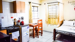 A compact hotel room with a kitchenette, a single bed, and a small dining table. - Affordable furnished studio apartment (Nairobi)