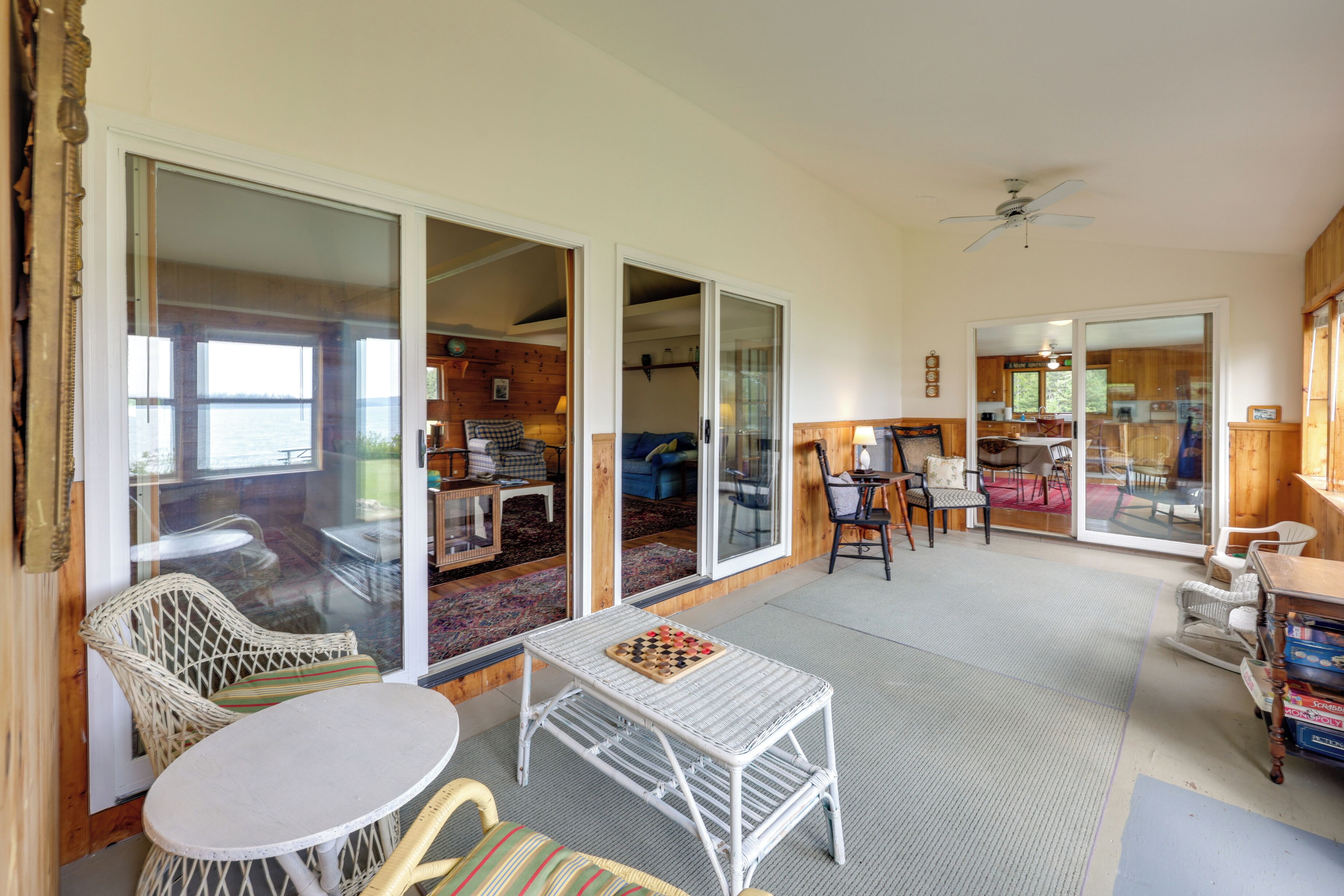 A spacious living area with a large sliding glass door leading to a balcony, wicker furniture, and a small table with a chessboard.