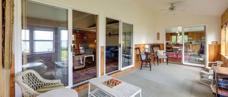 A spacious living area with a large sliding glass door leading to a balcony, wicker furniture, and a small table with a chessboard.