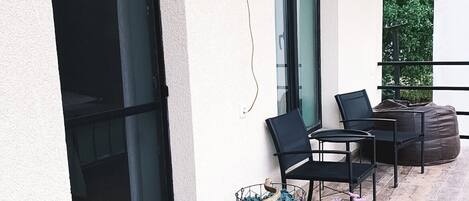 A balcony with a bicycle cart filled with flowers, a wall-mounted light fixture, and a seating area with chairs and a table.