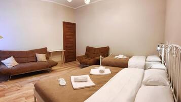 Ein Hotelzimmer mit braunem Sofa, einem Bett mit weißen Leinen, einem kleinen Tisch mit Lampe und einer Holztür.