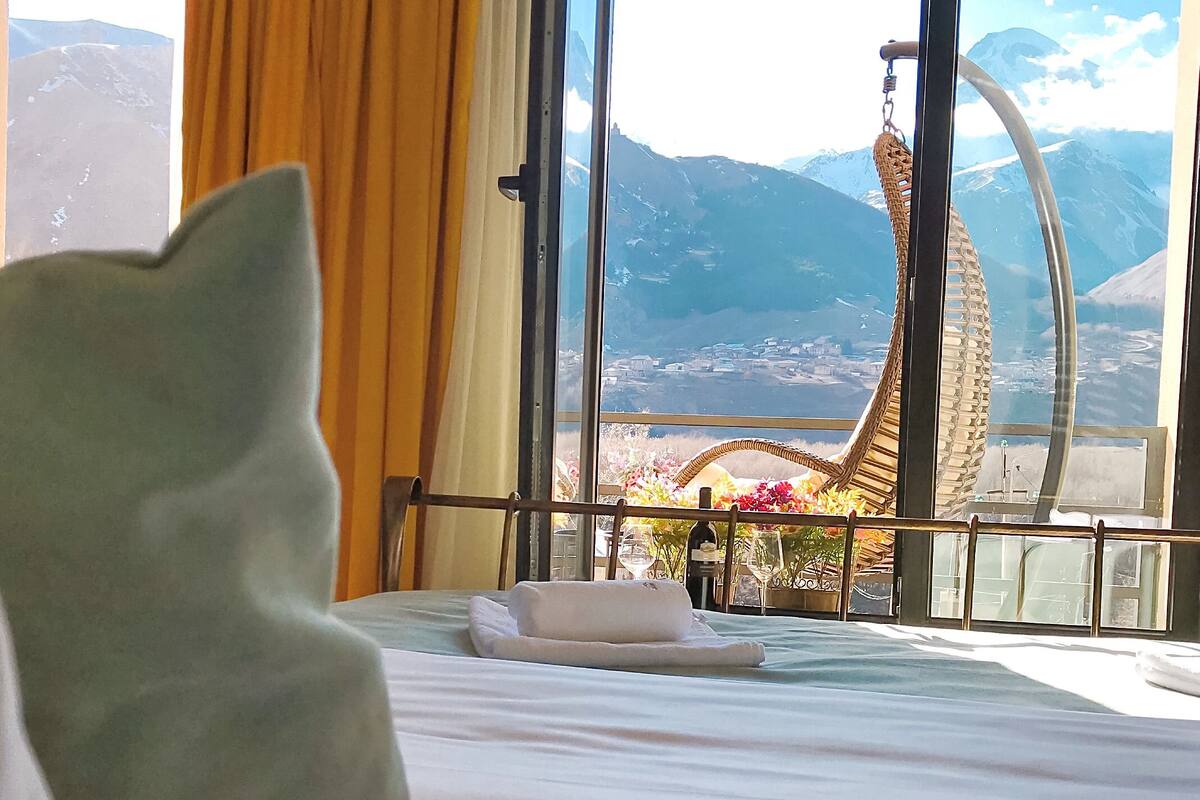 Una habitación de hotel con cama, vista a las montañas y balcón con barandilla.