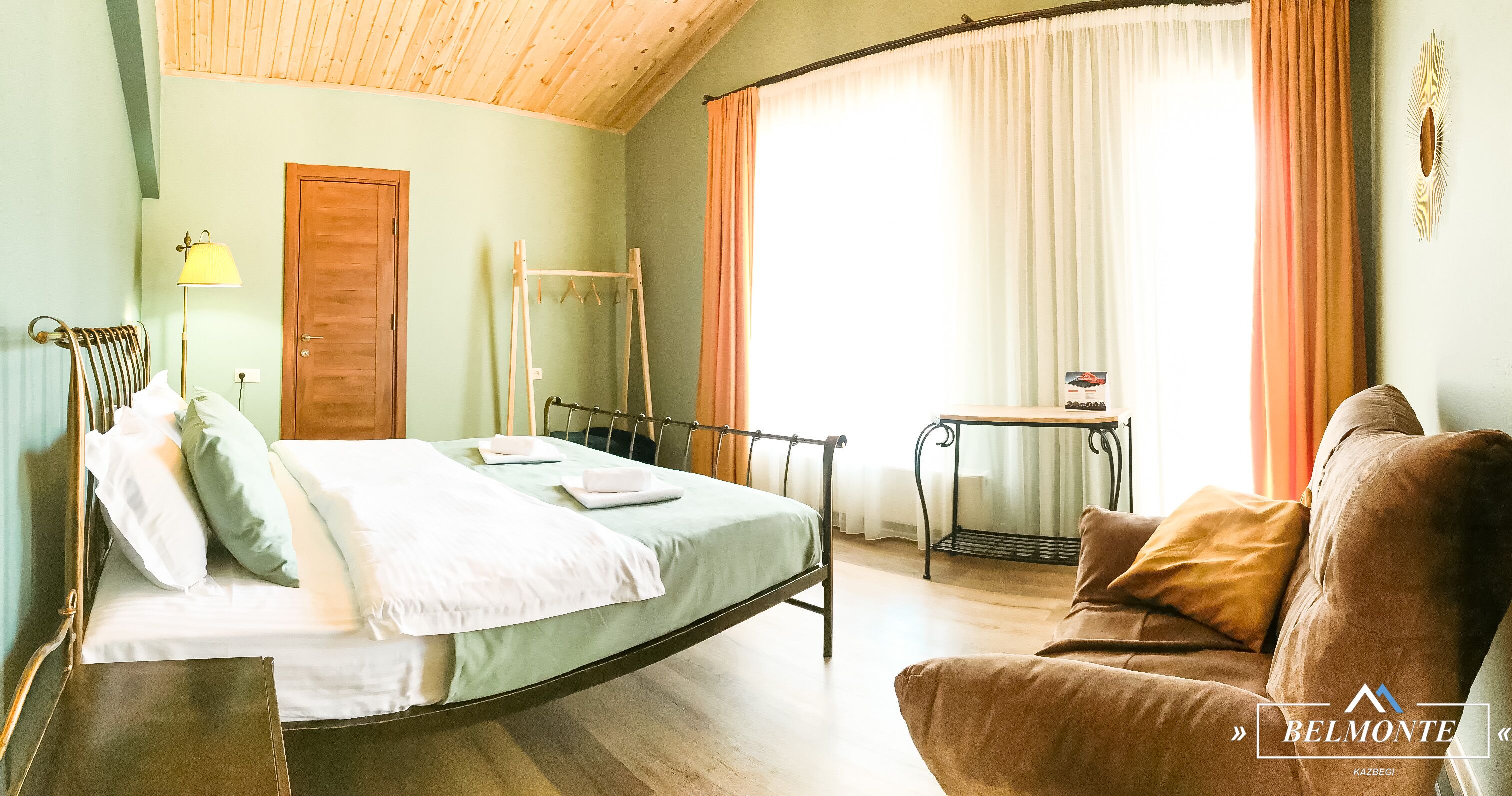 A bedroom with a bed, a wooden chair, a small table, and a sofa.
