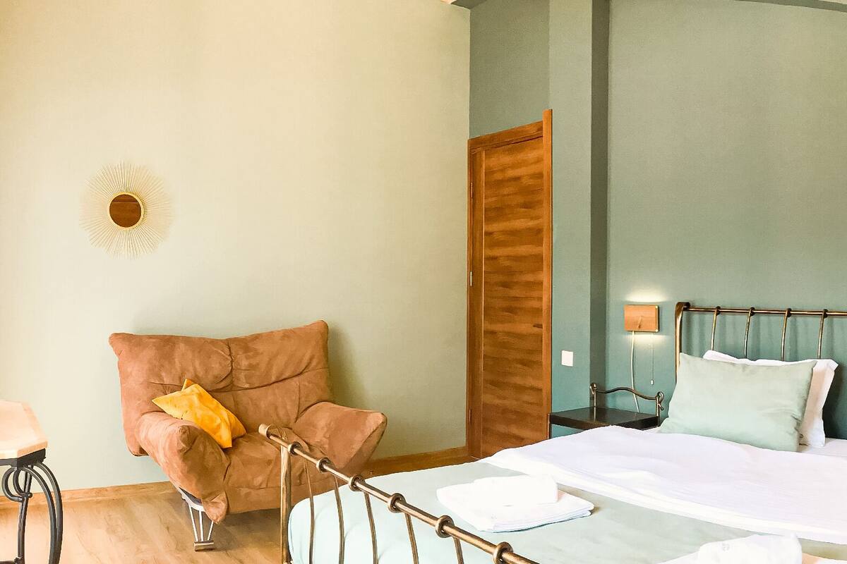 Un dormitorio con cama, una silla, una lámpara e iluminación en la pared.