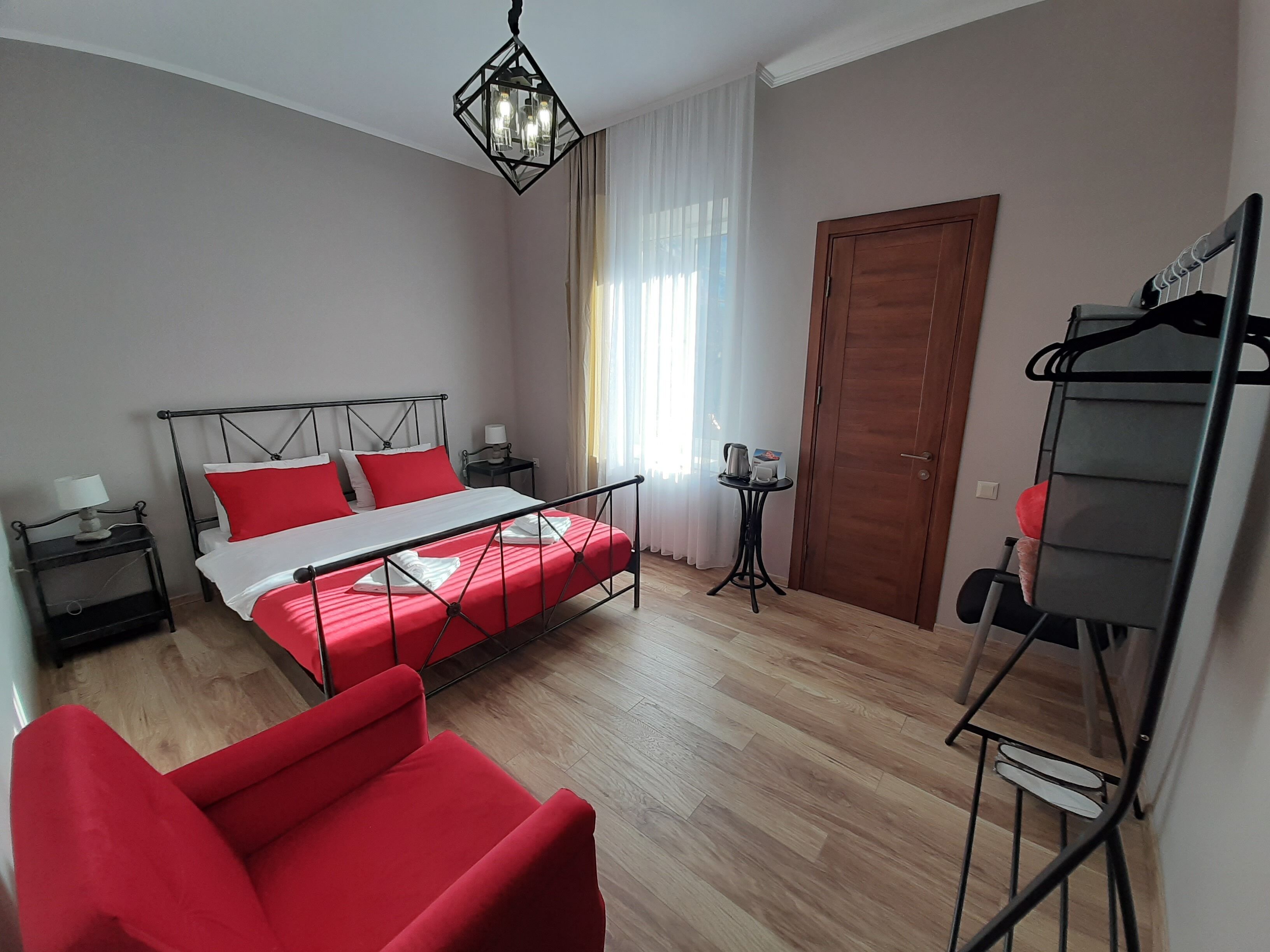Une chambre à coucher avec un lit, une chaise rouge, une petite table avec une bouilloire et une porte.