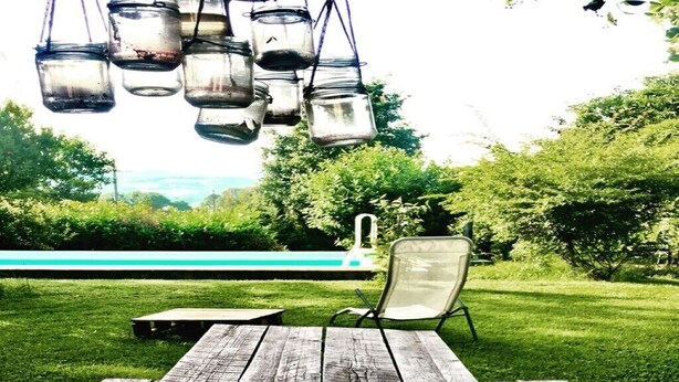 Une terrasse en bois avec une table en métal et une chaise, donnant sur une piscine et une végétation luxuriante.