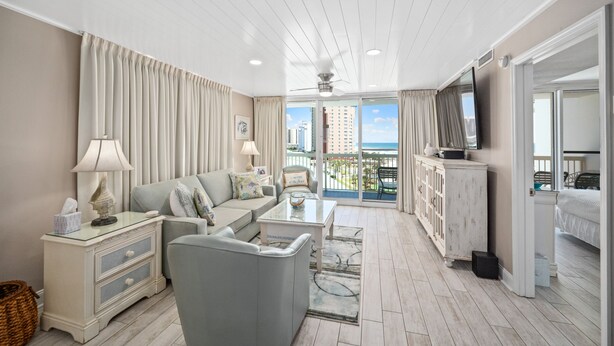 A spacious living room with a sofa, coffee table, and a television. The room has a balcony with a view of the city.