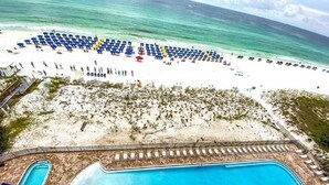 A beach with a swimming pool, lounge chairs, and a lifeguard tower.
