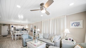 A modern living room with a dining area, a ceiling fan, and a kitchen in the background.