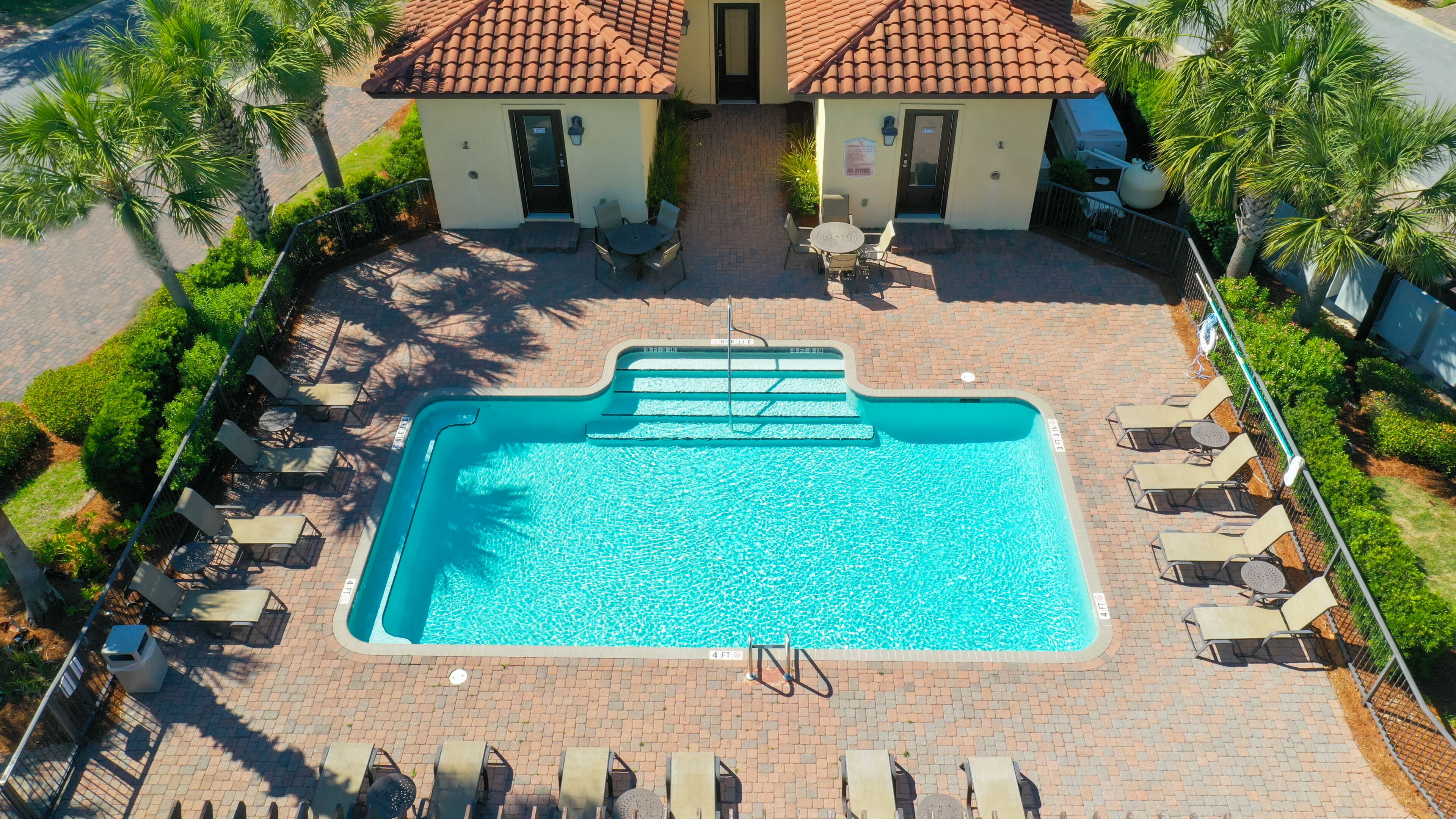 A rectangular swimming pool with a diving board, surrounded by lounge chairs and a small building with a tiled roof.