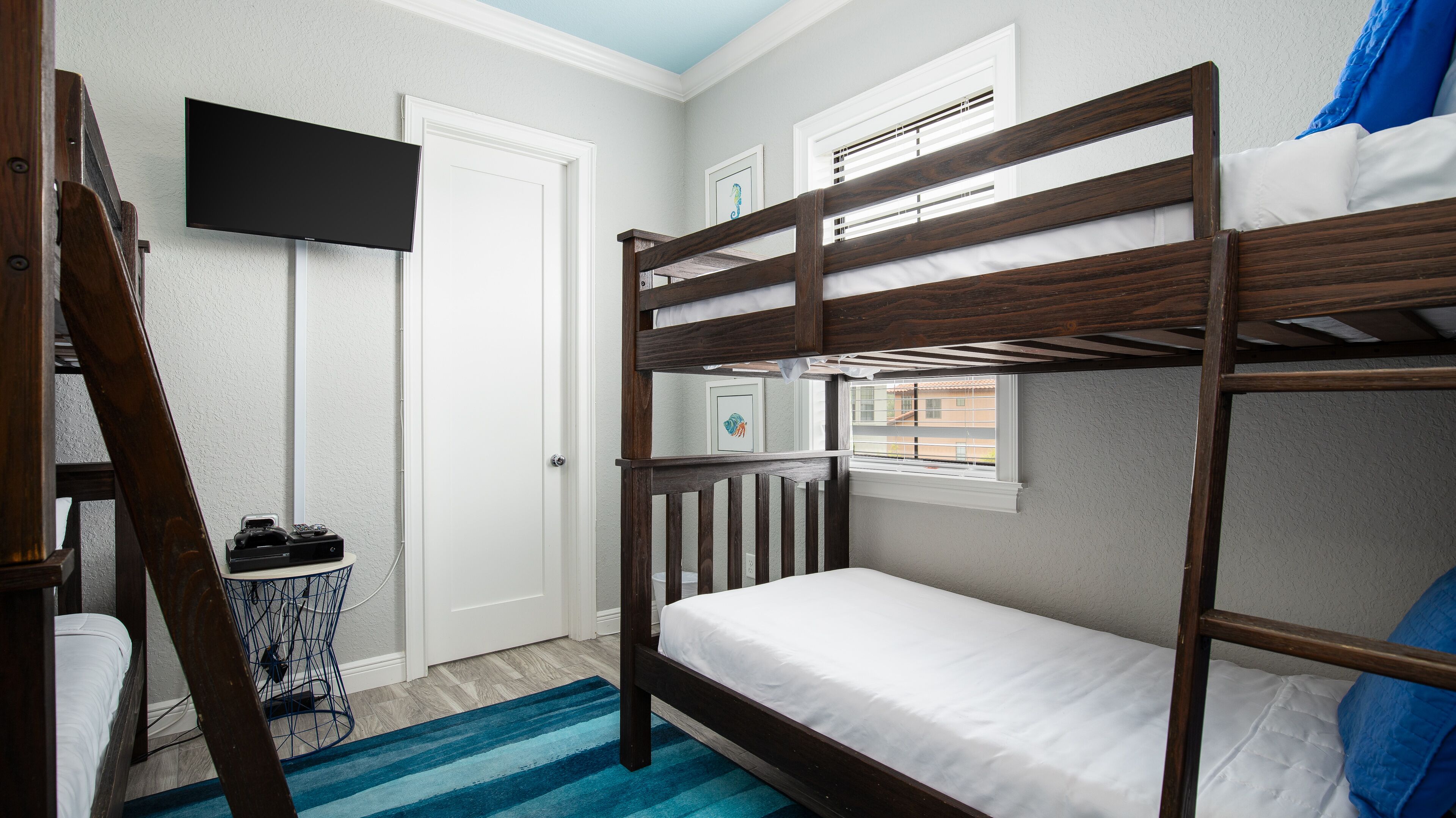 Een slaapkamer met stapelbed, een televisie aan de muur, een bureau met stoel en een raam met jaloezieën.