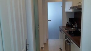 Um corredor estreito que dá para uma cozinha, com um relógio na parede.