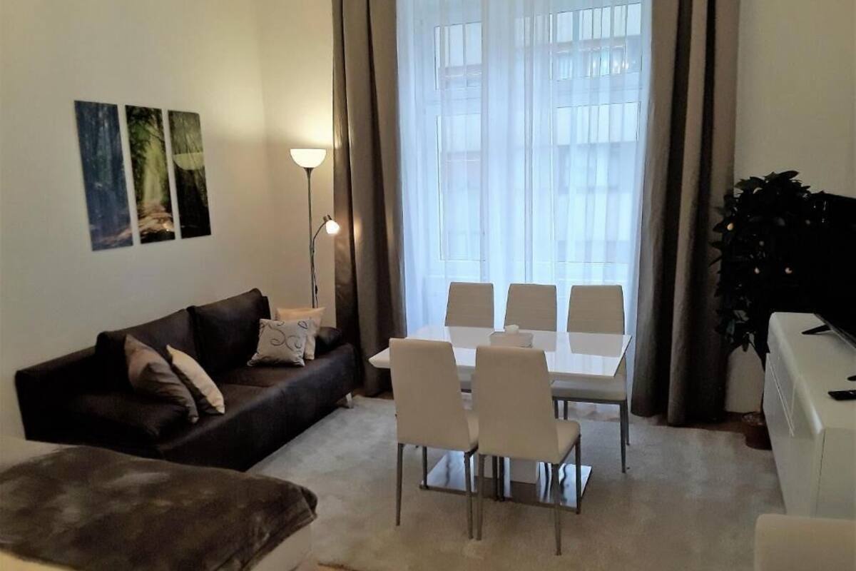 A living room with a sofa, a coffee table, a dining table with chairs, and a large window with curtains.