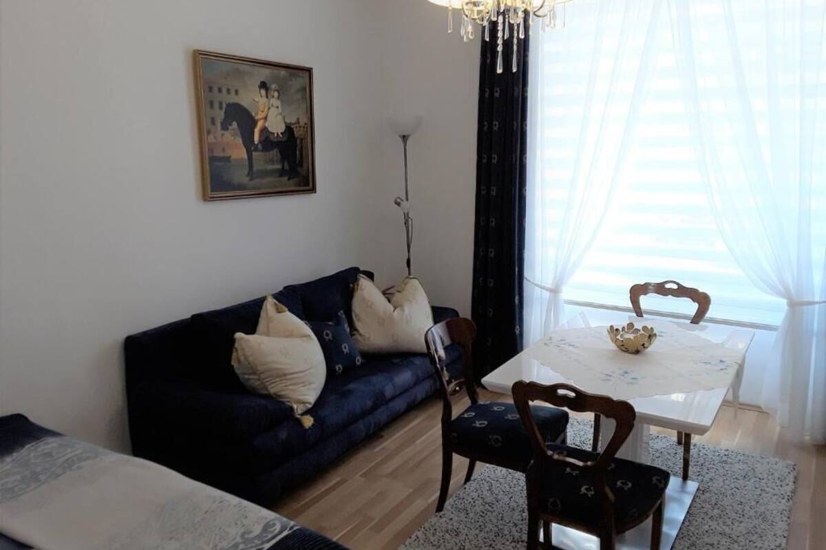 A living room with a dark blue sofa, a dining table with chairs, a chandelier, and a painting on the wall.