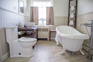 Un baño con inodoro, lavamanos, bañera y una ventana con cortinas.