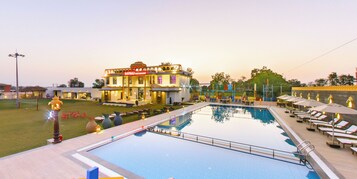Una piscina con sillas de descanso y sombrillas, un jardín césped y un edificio con un letrero.