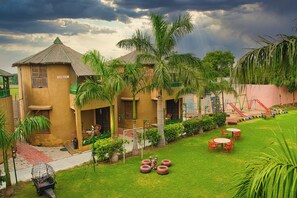 A two-story building with a sloped roof, a small porch, and a play area with slides and swings. - Hotel Natraj & Resort (Mansa)