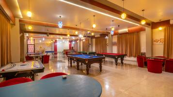 A billiards room with multiple tables and chairs, a pool table, and overhead lighting.