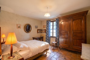 Een slaapkamer met een bed, nachtlampjes, een bureau, een stoel, een kledingkast en een raam met gordijnen.
