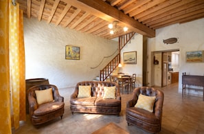 A rustic interior with leather armchairs, a wooden staircase, and a dining area.
