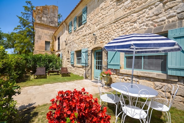 A stone building with a courtyard, outdoor seating, and a striped umbrella.