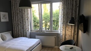 Ett sovrum med en säng, ett runt bord, två stolar, ett element och ett fönster med gardiner.