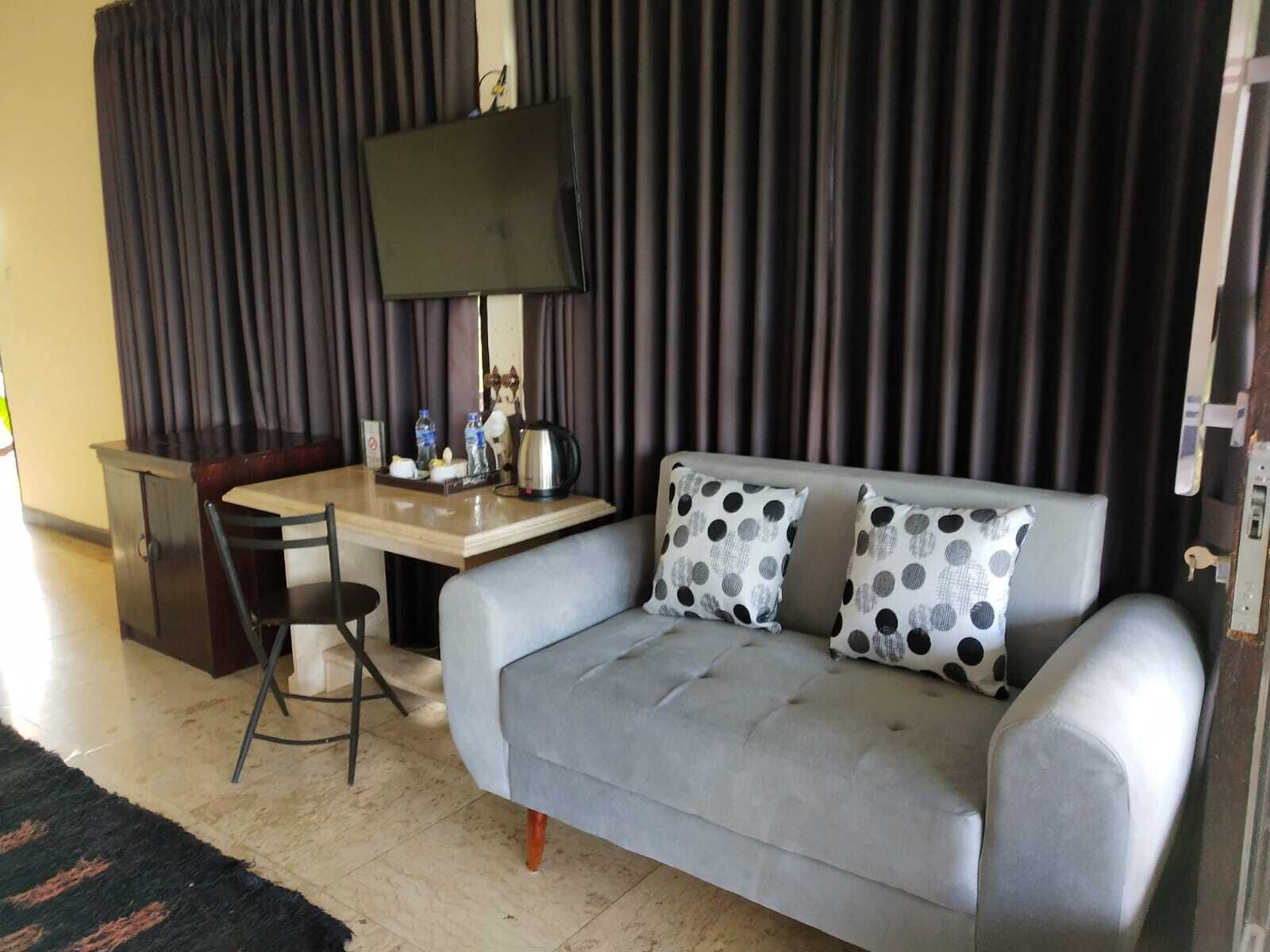 Una habitación con un sofá gris, un escritorio pequeño, una silla, un televisor y una cortina.