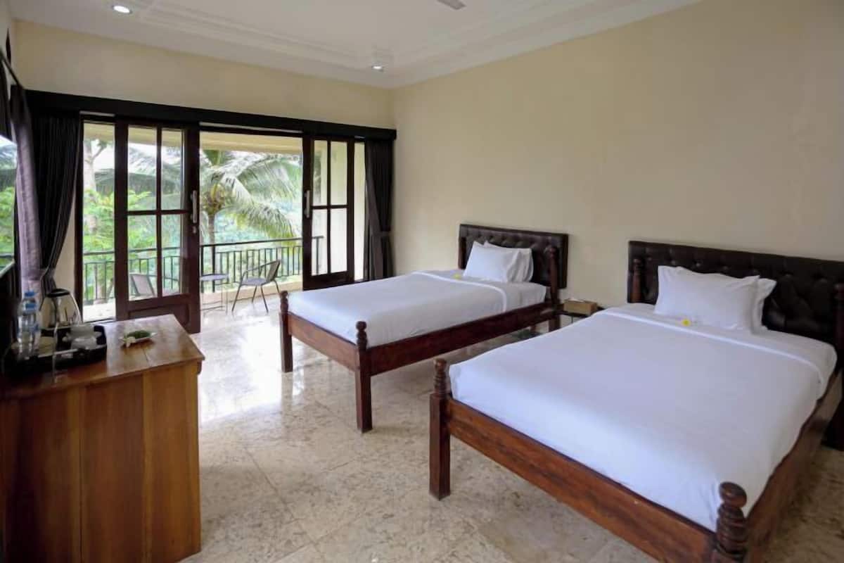A hotel room with two beds, a wooden desk, and a balcony with a view of palm trees.