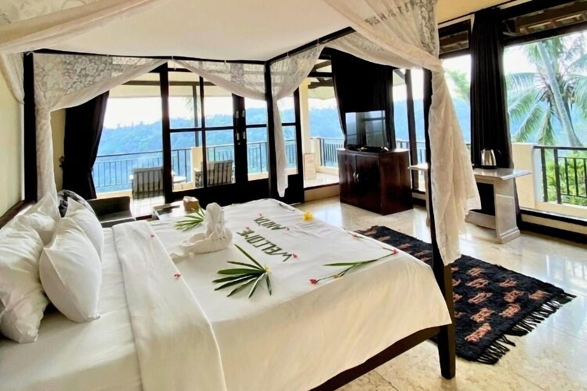 A bedroom with a bed, a ceiling fan, a nightstand, a window with a view, and a balcony.