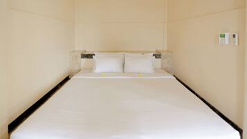 Una habitación de hotel con una cama individual, un cabecero de mármol y un termostato en la pared.