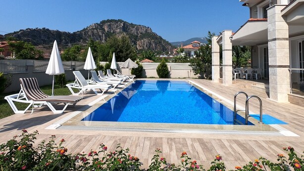 A pool area with lounge chairs and umbrellas, a clear blue pool, and a mountainous backdrop. - NEW LISTING!! BEAUTIFUL PRIVATE 5 BEDROOM VILLA RIGHT in CENTRE of DALYAN!!! (Dalyan Mahallesi / Ortaca)