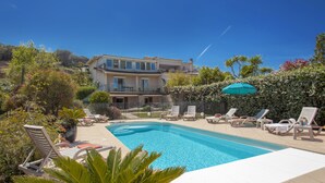 Una piscina con sillones de descanso y una casa grande al fondo.