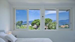 Un dormitorio con un ventanal que ofrece vistas a un lago, árboles y montañas distantes.