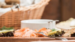 A wooden table with a plate of smoked salmon, a small bowl of sauce, and a basket in the background. - Hotel Klein Amsterdam (Friedrichstadt)