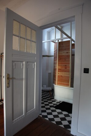 A hallway with a checkered floor, a white door with a brass handle, and a wooden panel wall. - Boutique Pension Ahoi (Wesselburenerkoog)