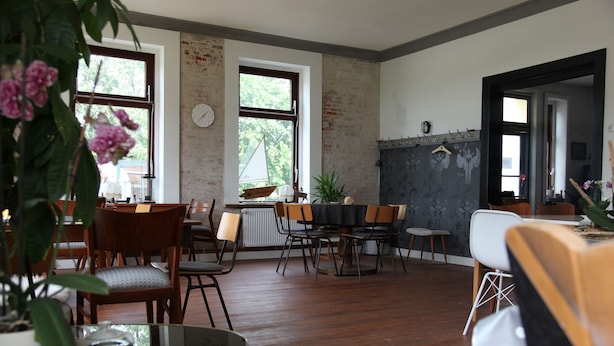 A dining area with wooden chairs and a table, large windows, and a brick wall. - Boutique Pension Ahoi (Wesselburenerkoog)