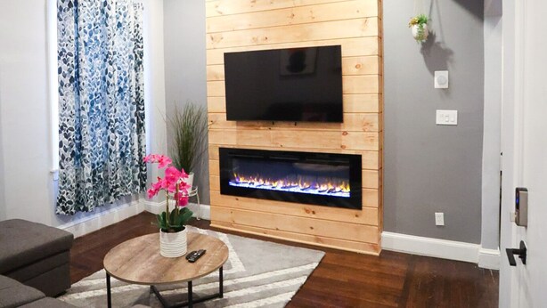 A modern living room with a fireplace, a ceiling fan, and a flat-screen TV mounted on a wooden wall. - Modern 3BR/ Close to Encore- Everett #2 (Everett)