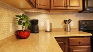 A kitchen with wooden cabinets, a brick backsplash, a coffee maker, a plant in a red pot, and a stainless steel microwave. - Modern 3BR/ Close to Encore- Everett #2 (Everett)