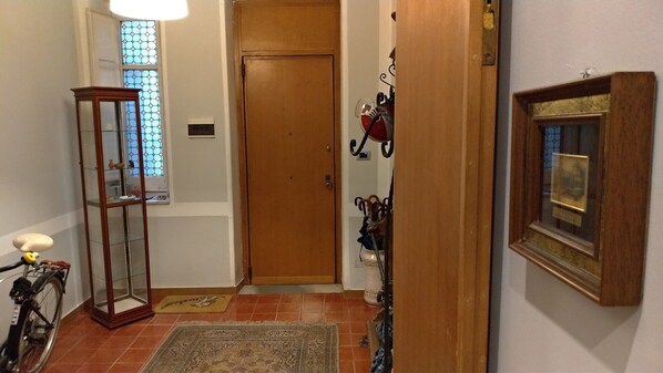 A hallway with a wooden door, a glass display cabinet, a bicycle, a rug, and a framed picture on the wall. - Il Genio del Porto - Mabbonath b&b (Palermo)