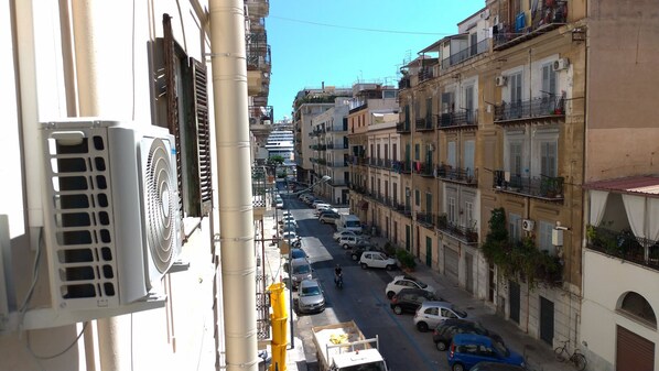 A narrow street lined with multi-story buildings, parked cars, and a large air conditioning unit on the left. - Il Genio del Porto - Mabbonath b&b (Palermo)