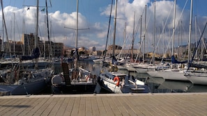 Un puerto deportivo con varias embarcaciones amarradas, cielo despejado y edificios al fondo.