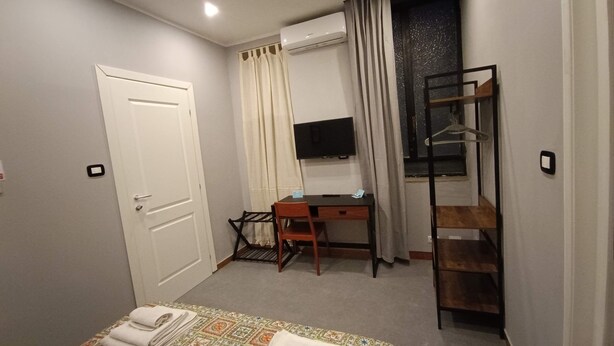 A bedroom with a bed, a desk, a TV, and a window with curtains. - Il Genio del Porto - Mabbonath b&b (Palermo)