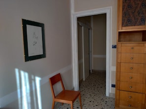 Un pasillo con una silla de madera, un cuadro enmarcado en la pared y un mueble de madera con cajones.