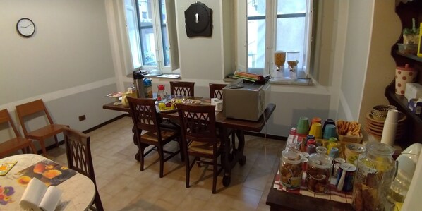 A dining area with a table set for four, chairs, a clock on the wall, and a window with blinds. - Il Genio del Porto - Mabbonath b&b (Palermo)
