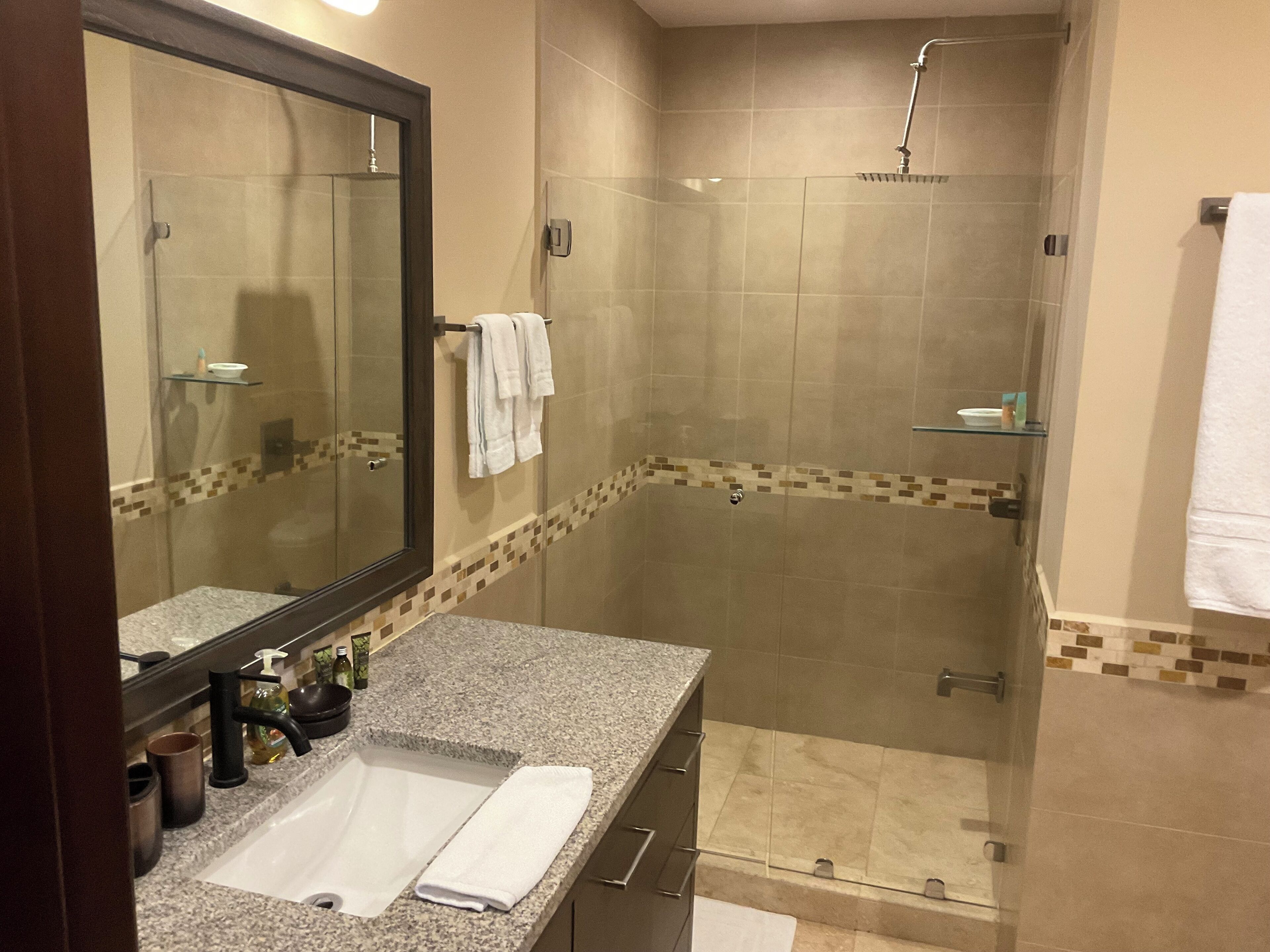 A modern bathroom with a granite countertop, a large mirror, a glass shower enclosure, and a tiled shower area.