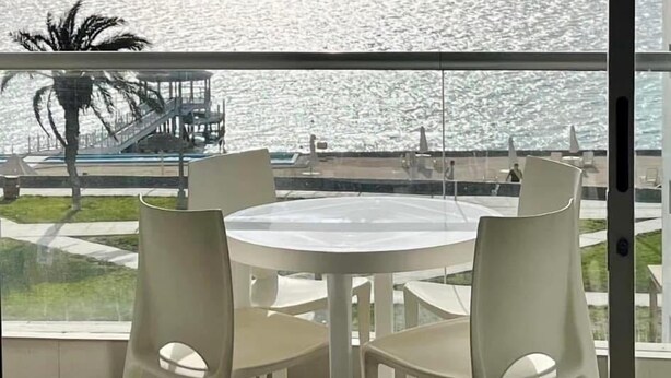 Un balcon avec une table et des chaises, donnant sur une étendue d’eau et un palmier.