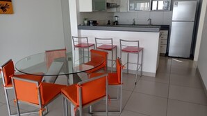 Une cuisine moderne avec des meubles blancs, un réfrigérateur en acier inoxydable et une table à manger en verre, assortie de chaises orange.