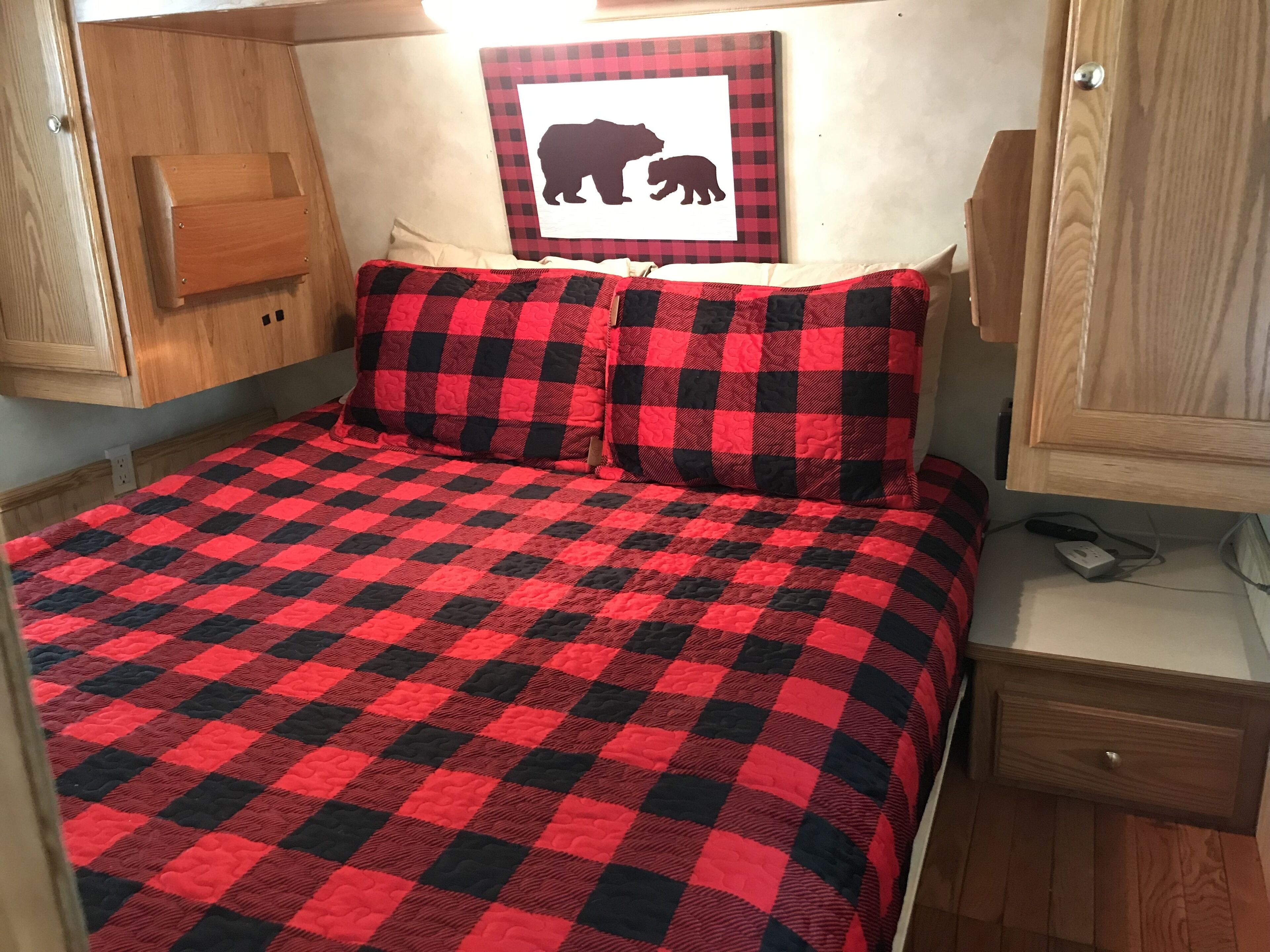 A bed with a red and black checkered bedspread, a pillow with a similar pattern, and a wall-mounted picture of a bear.